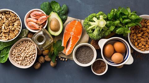 Mehrere fettreiche Lebensmittel auf einem Tisch, die gesund sind, wie Lachs und Avocado.