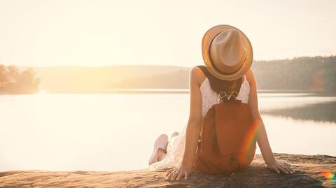Frau sitzt bei Sonnenuntergang auf einer Bank, sie ist entspannt und hat keine Körperspannung