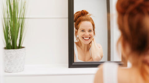 Eine Frau lächelt in einen Spiegel, nachdem sie eine Natural Skin Routine praktiziert hat