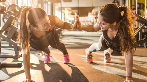 Zwei Frauen, die sich bei einem Liegestütz die Hände reichen