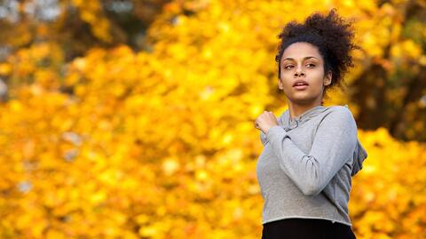 Frau joggt vor gelbem Herbstlaub, um sich auf die Erkältungs- und Grippesaison vorzubereiten