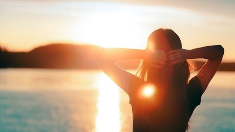 eine Frau, die vor einem Strand im Sonnenuntergang steht